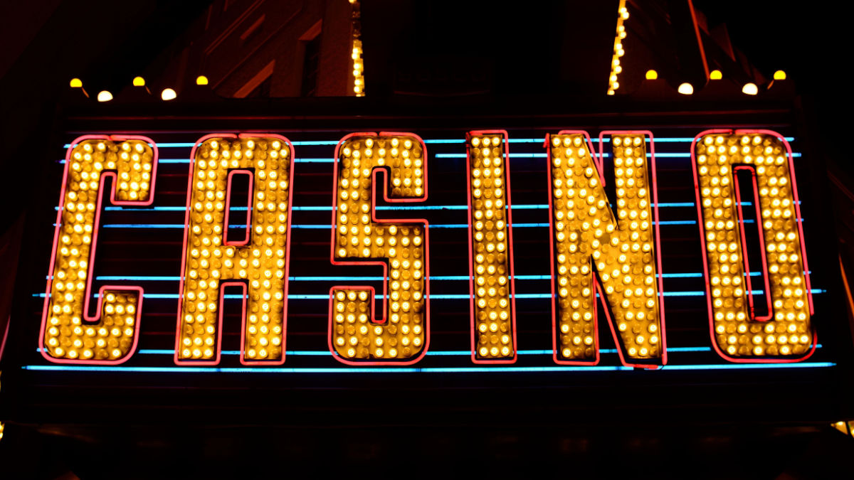 A brightly lit neon casino sign draws in renowned gamblers, creating a vibrant atmosphere.